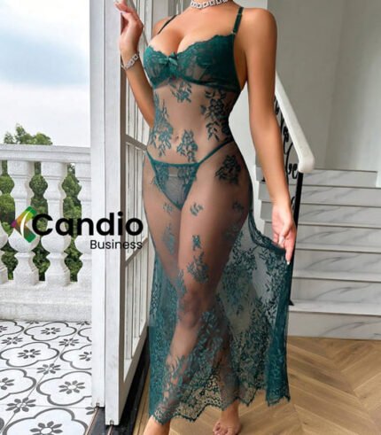 Une personne se tient debout sur un balcon extérieur blanc, vêtue du Sexy Ensemble de nuisette et string, une robe en dentelle verte transparente. L'arrière-plan comprend de la verdure et une balustrade blanche aux motifs ornementaux, avec le logo « Candio Business » partiellement visible sur le côté gauche de l'image.